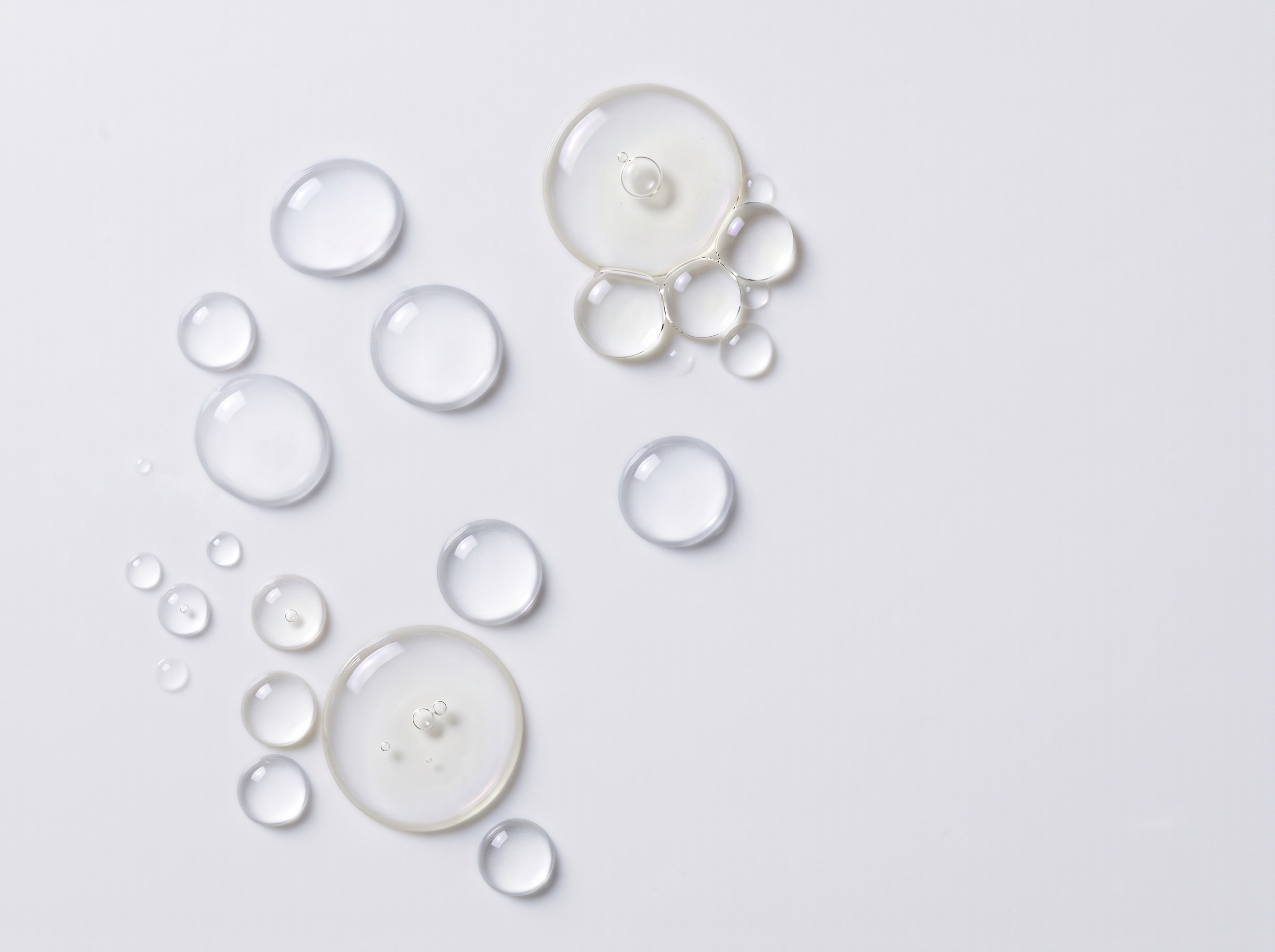 Clear water droplets and oil bubbles resting on a white surface