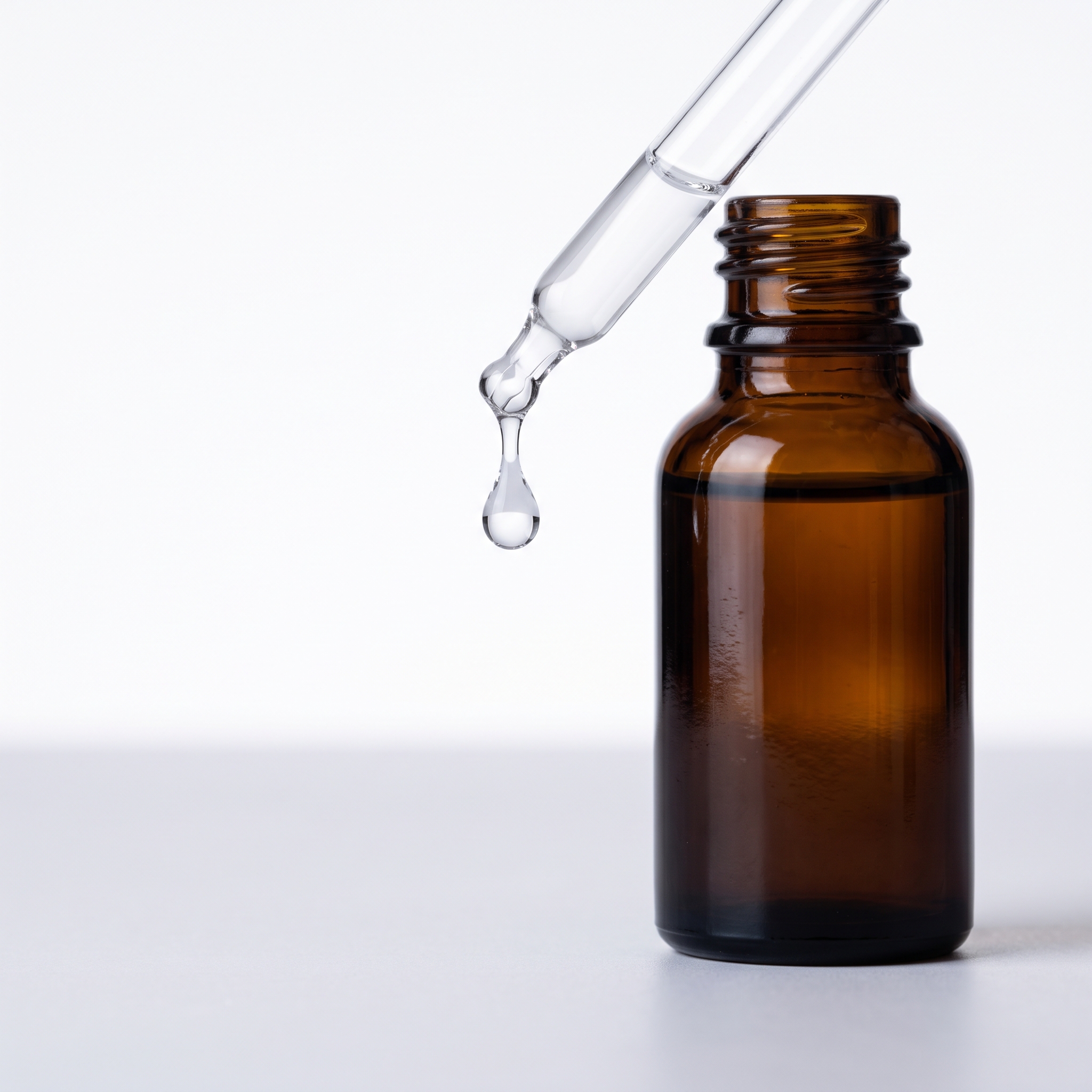 A glass pipette releasing one clear drop above an amber bottle