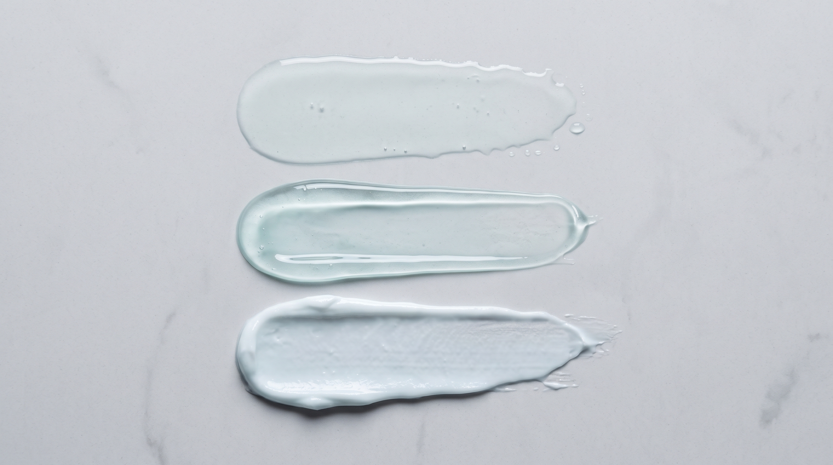 Three skincare swatches on stone: a watery toner, a gel serum and a dense cream